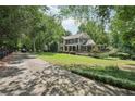 Scenic view of a charming two-story home with a covered front porch, deck, and expansive lawn surrounded by trees at 10875 Shagbark Trl, Roswell, GA 30075
