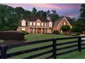 A brick two-story home has a manicured front yard with a black fence, plus a long driveway at dusk at 325 Edwards Brook Ln, Canton, GA 30115