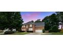 Dusk shot of a brick home with glowing windows, mature trees, and a long driveway, creating a warm ambiance at 285 Finsbury Park Ct, Suwanee, GA 30024