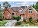 Striking brick home with arched doorway, dormer windows, manicured landscaping, and mature trees at 119 Kennemer Ct, Johns Creek, GA 30097