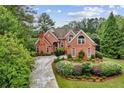 Charming brick home with a curved driveway, mature landscaping, and lush, green trees all around at 119 Kennemer Ct, Johns Creek, GA 30097
