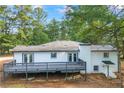 Back exterior featuring a spacious deck, white painted brick, and mature trees at 1377 Hill Sw Dr, Conyers, GA 30094