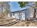 View of the home's rear, featuring light blue siding and a small patio area surrounded by trees at 2216 Marbut Farms Trce, Lithonia, GA 30058