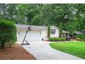 View of home with a two-car garage and basketball hoop in the driveway, surrounded by lush greenery at 3850 Beya Way, Atlanta, GA 30340