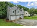 View of house featuring gray siding, a driveway, and surrounded by lush greenery at 11020 Knotty Pine Pl, Hampton, GA 30228
