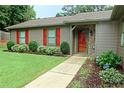 Close up on a charming single-story home featuring a stone accent wall, a red door, and a well-manicured lawn at 199 Candy Ln, Canton, GA 30115