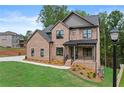Elegant two-story brick home with a covered porch, black trim windows, and lush lawn at 6120 Hutchins Dr, Buford, GA 30518