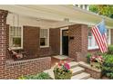 Inviting front porch features a swing and brick columns, complemented by vibrant flowers and a charming American flag at 1371 N Highland Ne Ave, Atlanta, GA 30306