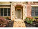 Close-up of a stone-arched front door with decorative shrubs, creating an inviting entrance to this lovely home at 13042 Dartmore Ave, Alpharetta, GA 30005