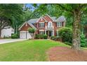 Brick home boasts a manicured lawn, mature trees, and a convenient two-car garage at 1115 Ballington Dr, Cumming, GA 30041
