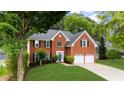 Charming two-story brick home featuring a lush, green lawn, mature trees, and a driveway to a two-car garage at 10865 Misty Moon Ct, Alpharetta, GA 30022