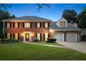 Elegant two-story red brick home with manicured lawn and a driveway, illuminated at dusk at 2903 Ashebrooke Ne Dr, Marietta, GA 30068