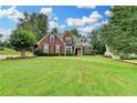 Beautiful two-story brick home with a well-manicured lawn and mature trees on a sunny day at 5036 Weatherstone Drive, Buford, GA 30519