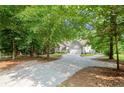View of a long concrete driveway leading to a gray home with an attached garage, surrounded by mature trees and lush greenery at 2730 Samples Rd, Cumming, GA 30041