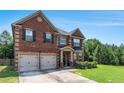 Beautiful red brick home with a two-car garage, a manicured lawn, and mature trees providing ample shade at 10044 Cormac St, Jonesboro, GA 30238