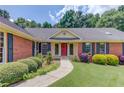 Lovely brick home with lush landscaping, dark shutters, and a welcoming front entrance with a red door at 3550 Miller Farms Ln, Peachtree Corners, GA 30096