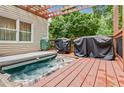 Hot tub on wood deck with an open pergola featuring an outdoor grill, and view of the wooded surroundings at 3605 Hickory Se Cir, Smyrna, GA 30080