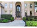 Close-up of the grand front entrance, featuring an arched doorway, brick accents, and manicured greenery at 8430 Merion Drive, Duluth, GA 30097