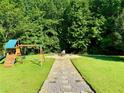 Large backyard with a playset, chairs around a fire pit, and an abundance of lush trees at 5388 Silver Springs Dr, Sugar Hill, GA 30518
