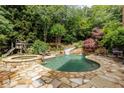 Backyard oasis with a stone-surrounded pool, waterslide, hot tub, and lush landscaping at 5284 Vernon Springs Nw Trl, Sandy Springs, GA 30327