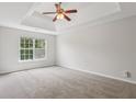 Large main bedroom with carpet, tray ceiling, ceiling fan, and a view of the backyard at 1025 Pebble Creek Trl, Suwanee, GA 30024