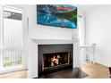 Cozy living room featuring a fireplace, large TV, hardwood floors, white walls, and a small table near the window at 10862 Serenbe Ln, Chattahoochee Hills, GA 30268