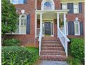 Close up of a red brick house entrance with white columns, black door, brick steps and green bushes at 1620 Silverleaf Way, Alpharetta, GA 30005