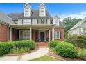A classic two-story brick home featuring a covered porch with chairs and manicured hedges at 4653 Glory Maple Trce, Powder Springs, GA 30127