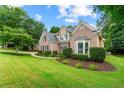 Beautifully landscaped front yard of a brick home with a curved driveway, mature trees, and green lawn at 1995 Settindown Dr, Roswell, GA 30075