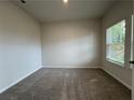 A carpeted bedroom featuring neutral walls, a window for natural light, and a view to the backyard at 1601 Dosk Ave, Lawrenceville, GA 30044