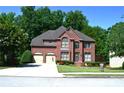 Charming two-story red brick home with arched windows, attached garage and manicured front lawn, surrounded by mature trees at 3930 Regal Oaks Dr, Suwanee, GA 30024