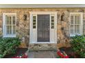 Inviting front entrance with a stone surround, classic black door, and decorative sconces at 220 Hollyridge Dr, Roswell, GA 30076