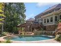 A luxurious backyard oasis features a stone patio, cascading waterfall, covered deck, and large inground pool at 217 Fernwood Pl, Woodstock, GA 30188