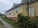 Side view of home with yellow wood siding, brick foundation, and overgrown landscape at 854 Mcdonough Se Blvd, Atlanta, GA 30315