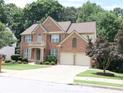 Traditional brick home with a two-car garage, front yard landscaping, and a second-story balcony at 5157 Wellisford Ct, Suwanee, GA 30024
