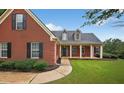 Inviting red brick home featuring a covered porch, dormer windows, and lush landscaping at 65 Pecan Ln, Oxford, GA 30054