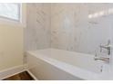 Clean bathroom featuring a tub with white marble tiling, light yellow walls, and vinyl wood flooring at 1885 N Druid Hills Ne Rd, Atlanta, GA 30319