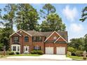 Charming two-story red brick home featuring a two-car garage, manicured landscaping, and mature trees at 5745 Crystal Springs Way, Powder Springs, GA 30127