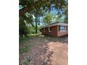Exterior view of single-story home with brick siding, green metal roof, and partially wooded lot at 10591 Flat Shoals Rd Rd, Covington, GA 30016