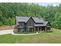 Aerial view of a dark modern farmhouse boasting a three car garage, basketball court, lush lawn and woods at 2100 Mountain Cove Ct, Woodstock, GA 30188