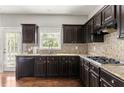 Well-appointed kitchen features dark cabinetry, granite countertops, a stylish mosaic backsplash, and stainless steel appliances at 2251 Fall Creek Lndg, Loganville, GA 30052