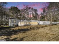 Stunning modern home with a large yard and unique architecture, surrounded by mature trees and a beautiful colorful sky at 115 Wilkins Rd, Fayetteville, GA 30214