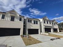 Newly built townhomes with brick facades, black garages, concrete driveways, and bright blue skies at 1935 Westwind Street # 157, Lawrenceville, GA 30043