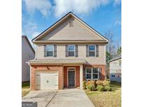 Two-story house with brick and beige siding, a two-car garage, and a well-manicured lawn at 11945 Lovejoy Crossing Way, Hampton, GA 30228