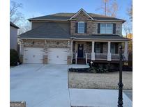 Inviting two-story home featuring a two-car garage, stone accents, and a charming front porch perfect for relaxing at 1320 Newbridge Cir, Buford, GA 30519
