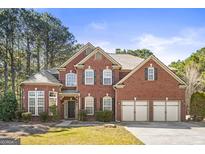 Stunning red brick home featuring a three car garage, manicured lawn, and mature trees at 100 Windmeadow Way, Fayetteville, GA 30214