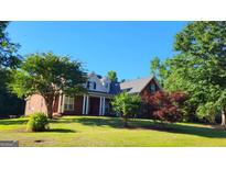 Traditional brick home featuring a manicured lawn, mature landscaping, and a welcoming front porch at 35 Abelia Dr, Covington, GA 30014