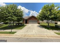 Charming one-story brick home with a two-car garage, lush lawn, and mature shade trees at 1687 Blue Heron Way, Hampton, GA 30228