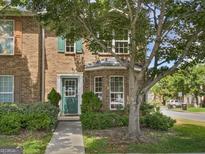 Charming brick townhome features a green front door, lush landscaping, and a mature shade tree in a residential neighborhood at 11403 South Grove Dr, Hampton, GA 30228