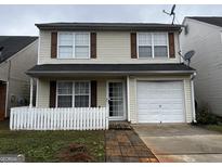 Charming two-story home with tan siding, brown shutters, a white picket fence, and an attached one-car garage at 419 Kara Ln, Mcdonough, GA 30253